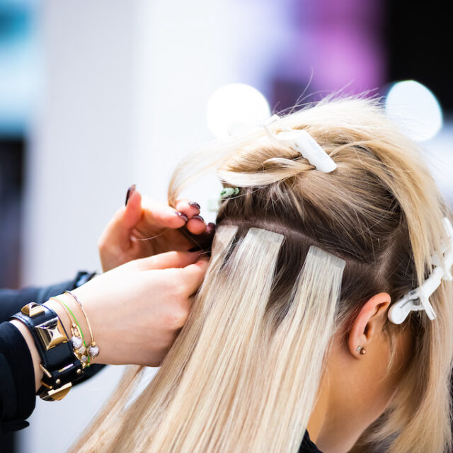 Professional hairdresser making hair extensions for blonde girl in a beauty salon