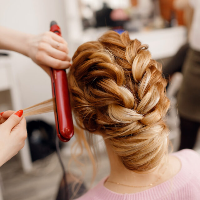 Woman hairdresser making hairstyle to blonde girl in beauty salon.