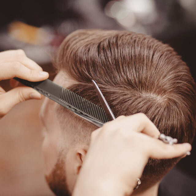 Close-up, master hairdresser does hairstyle with scissors comb. Concept Barbershop.