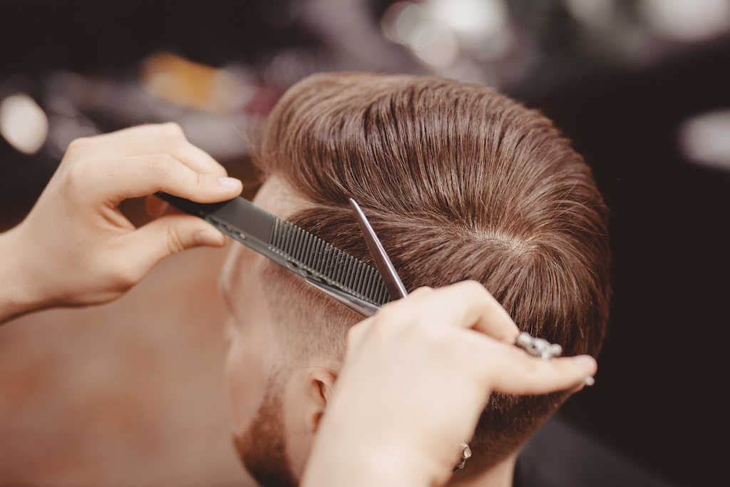 Close-up, master hairdresser does hairstyle with scissors comb. Concept Barbershop.