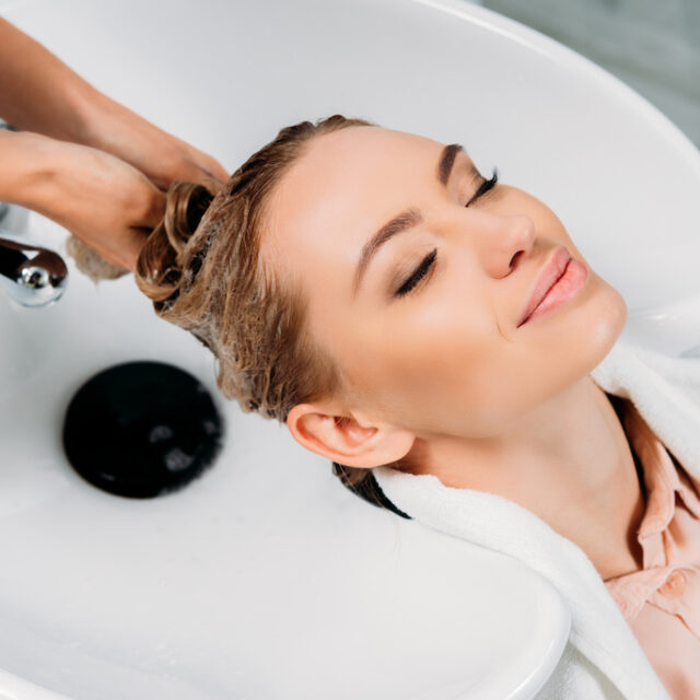 cropped image of hairdresser washing hair for customer with shampoo